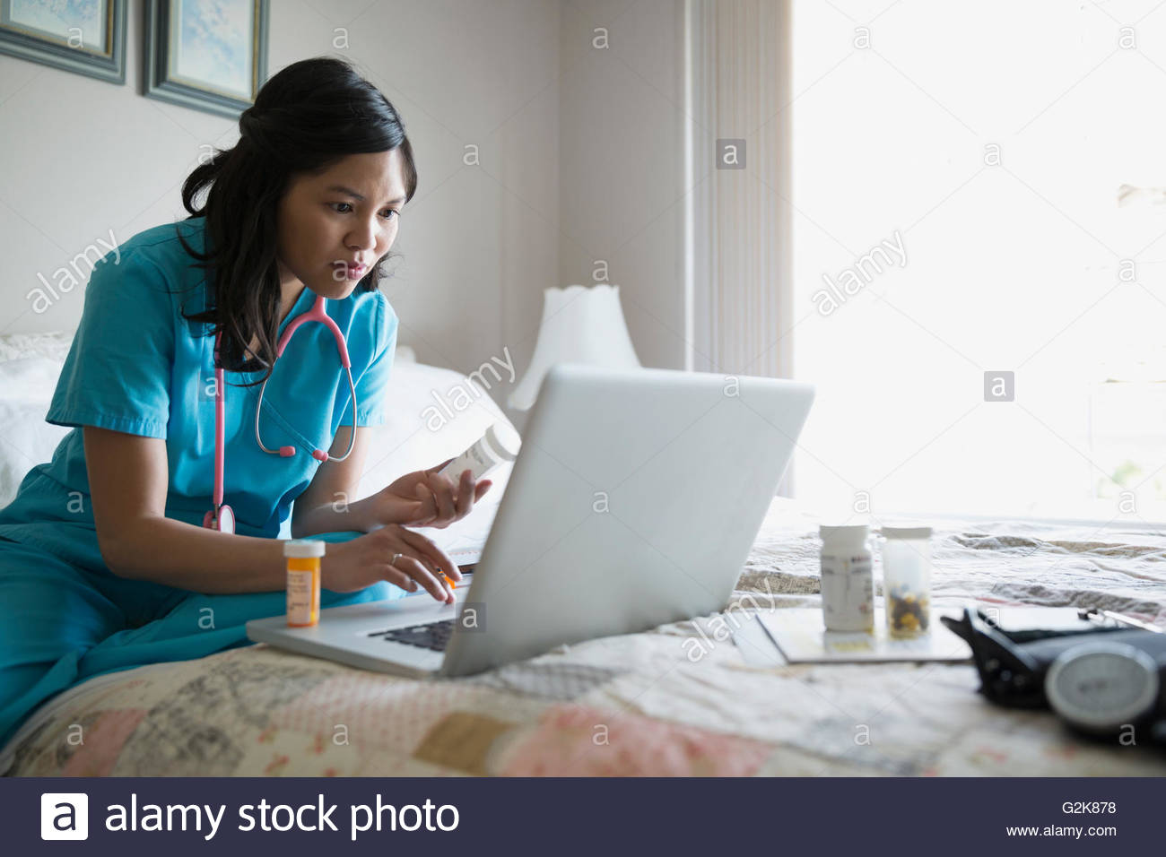 Home caregiver with prescriptions using laptop on bed Stock Photo