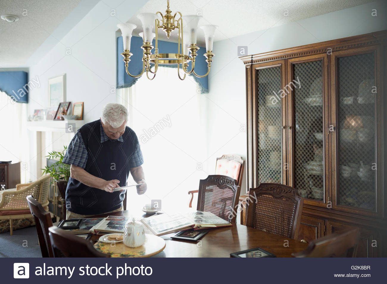 Senior man using digital tablet at dining table with photograph albums Stock Photo