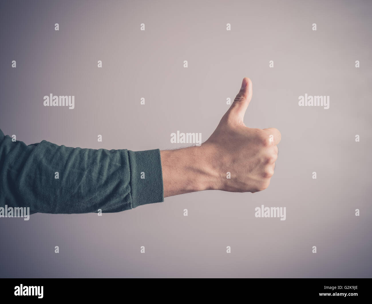 A young man wearing a green top is giving the thumbs up sign Stock Photo