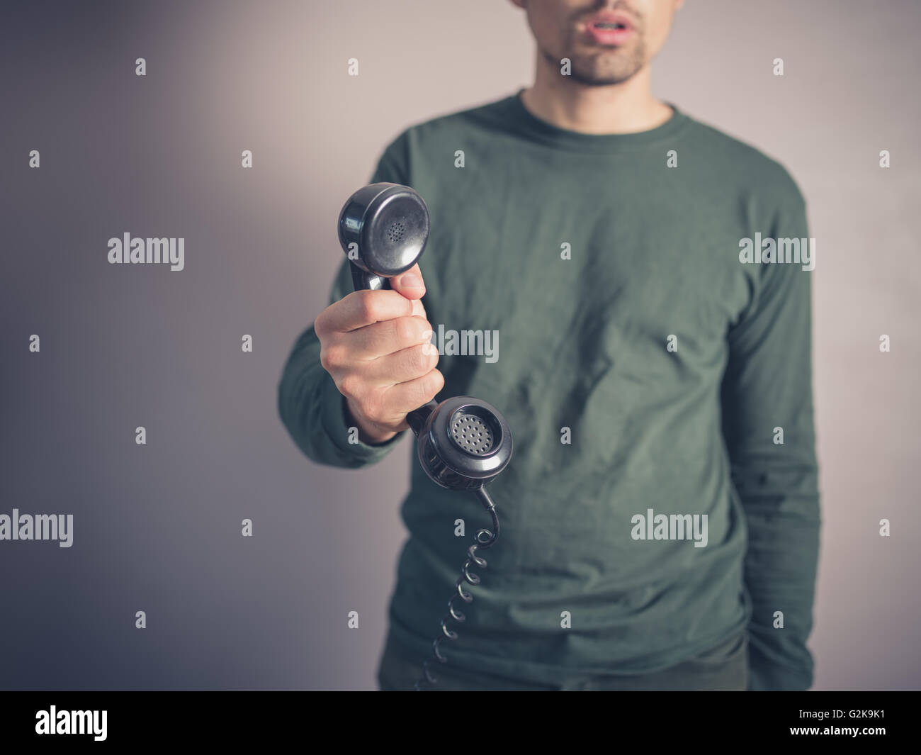 A concerned and worried looking young man is holding the receiver of a vintage rotary phone Stock Photo