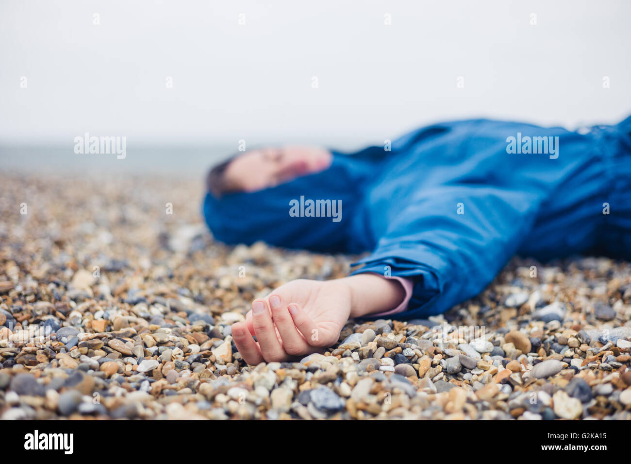 An unconscious woman is lying on a shingle beach Stock Photo