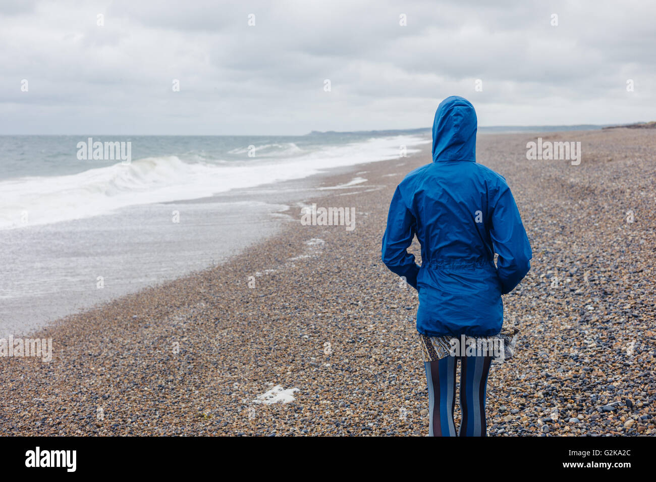 A young woman wearing a blue waterproof jacket is walking on the beach ...