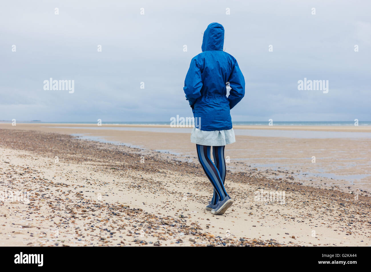 A young woman wearing a blue waterproof jacket is walking on the beach ...