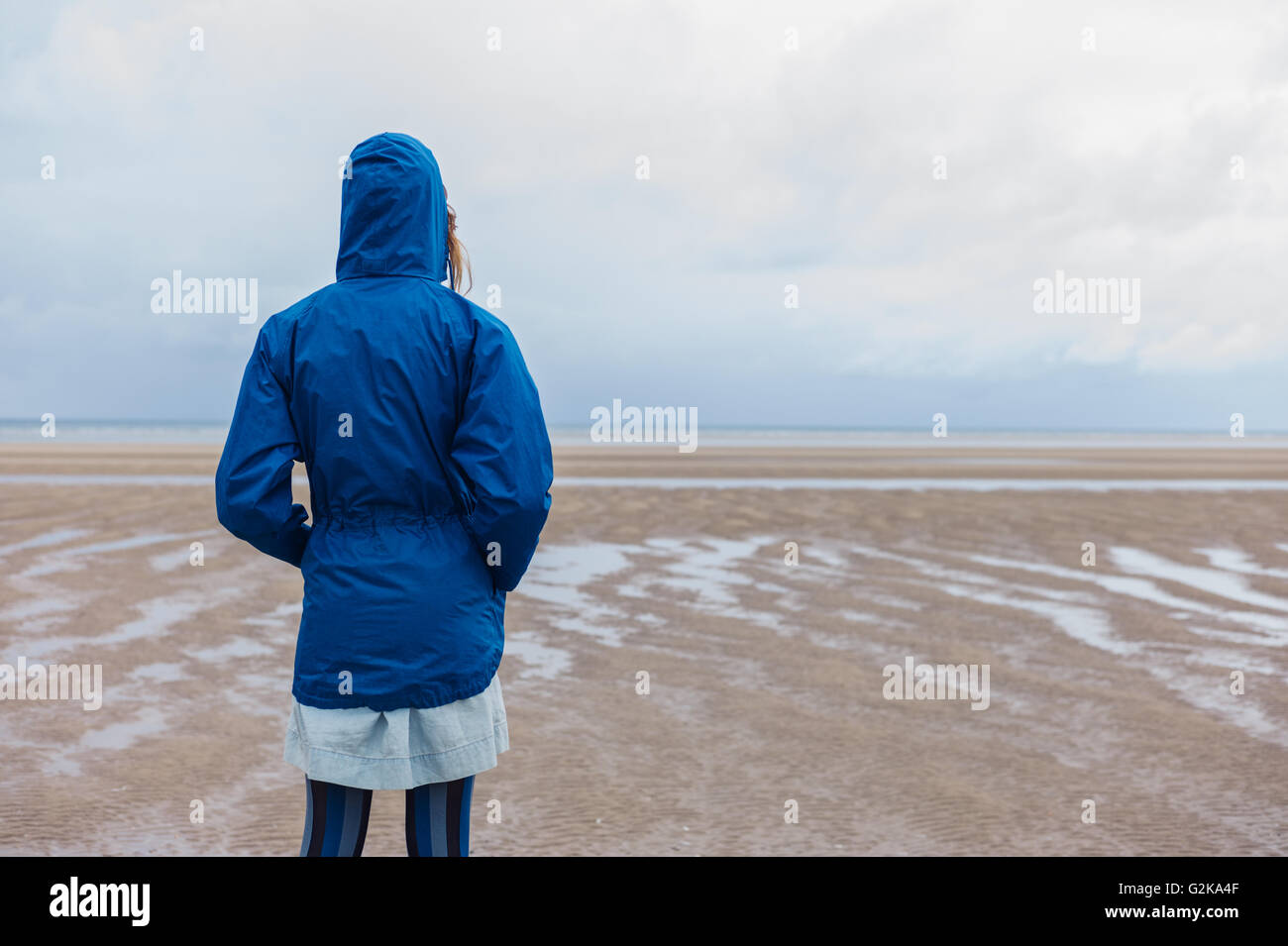 A young woman wearing a blue waterproof jacket is walking on the beach ...
