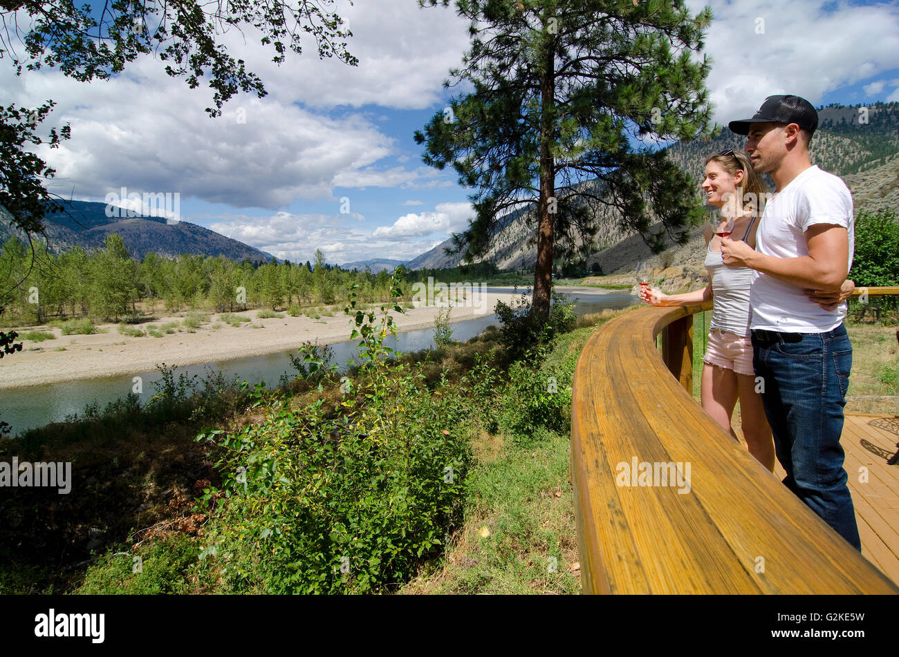 Young couple savours view Similkameen River while sampling wine from Forbidden Fruit Winery near Cawston in Similkameen region Stock Photo