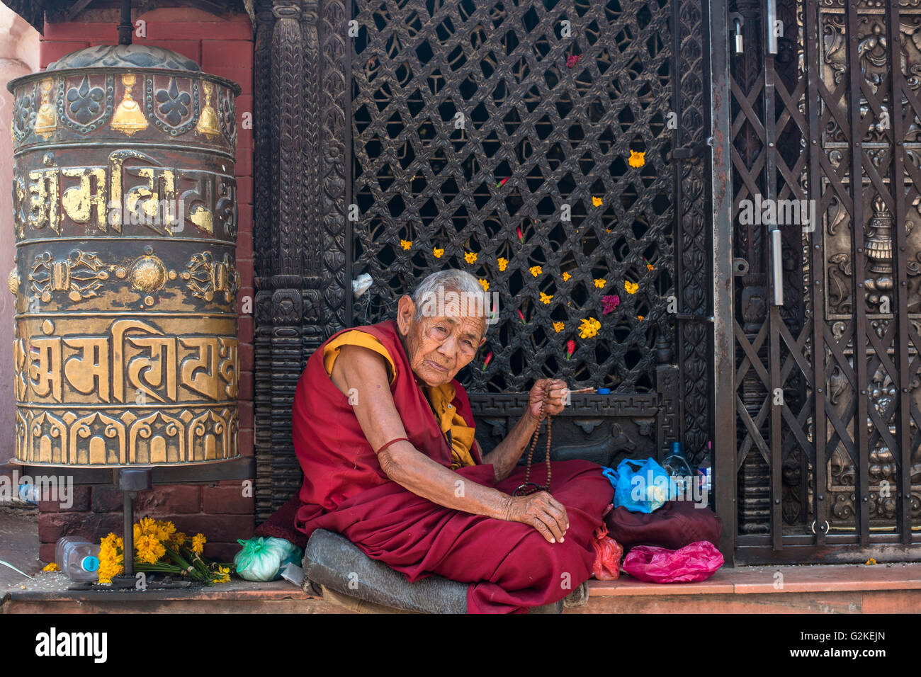 Old woman with prayer beads, Buddhist nun sitting next to a prayer wheel, Boudha Stupa, Kathmandu, Nepal Stock Photo