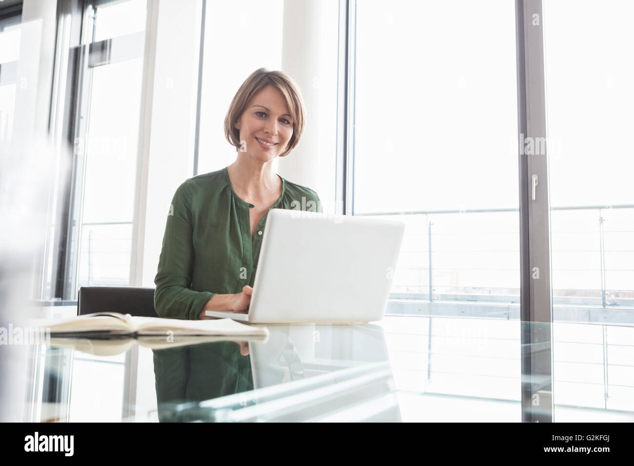 Portrait of smiling businesswoman working on laptop at office desk Stock Photo
