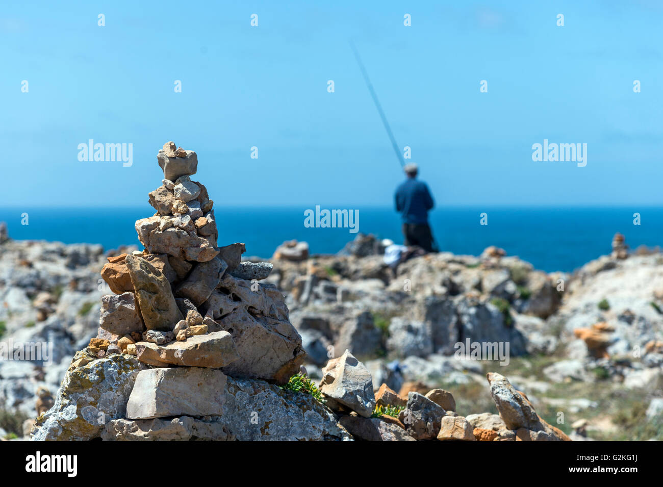 Portugal, Algarve, Sagres, cairn at coast, angler in the background Stock Photo