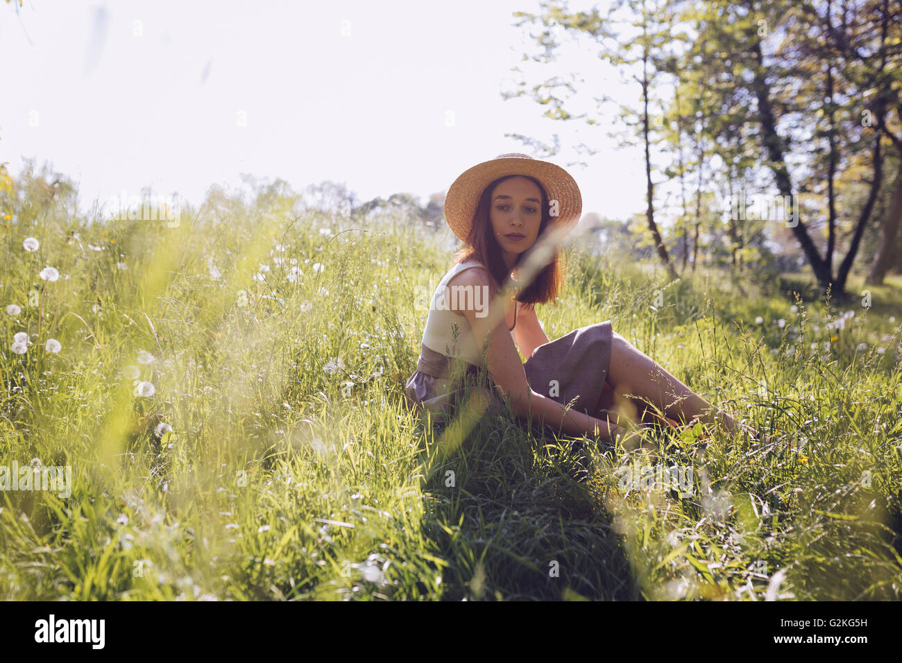 Young woman wearing straw hat sitting on a meadow Stock Photo - Alamy