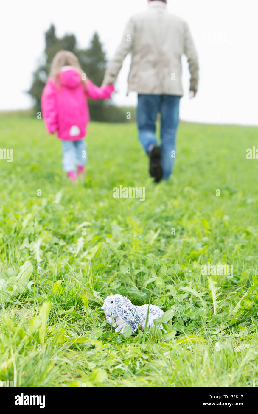 Cuddly toy lying on meadow while man going away with little girl Stock Photo