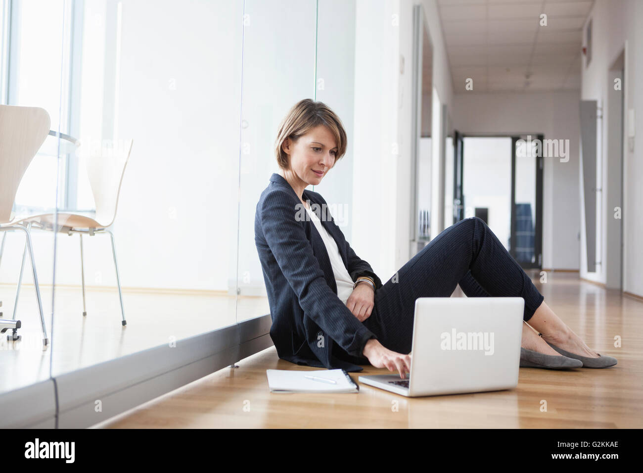 Businesswoman sitting on office floor using laptop Stock Photo