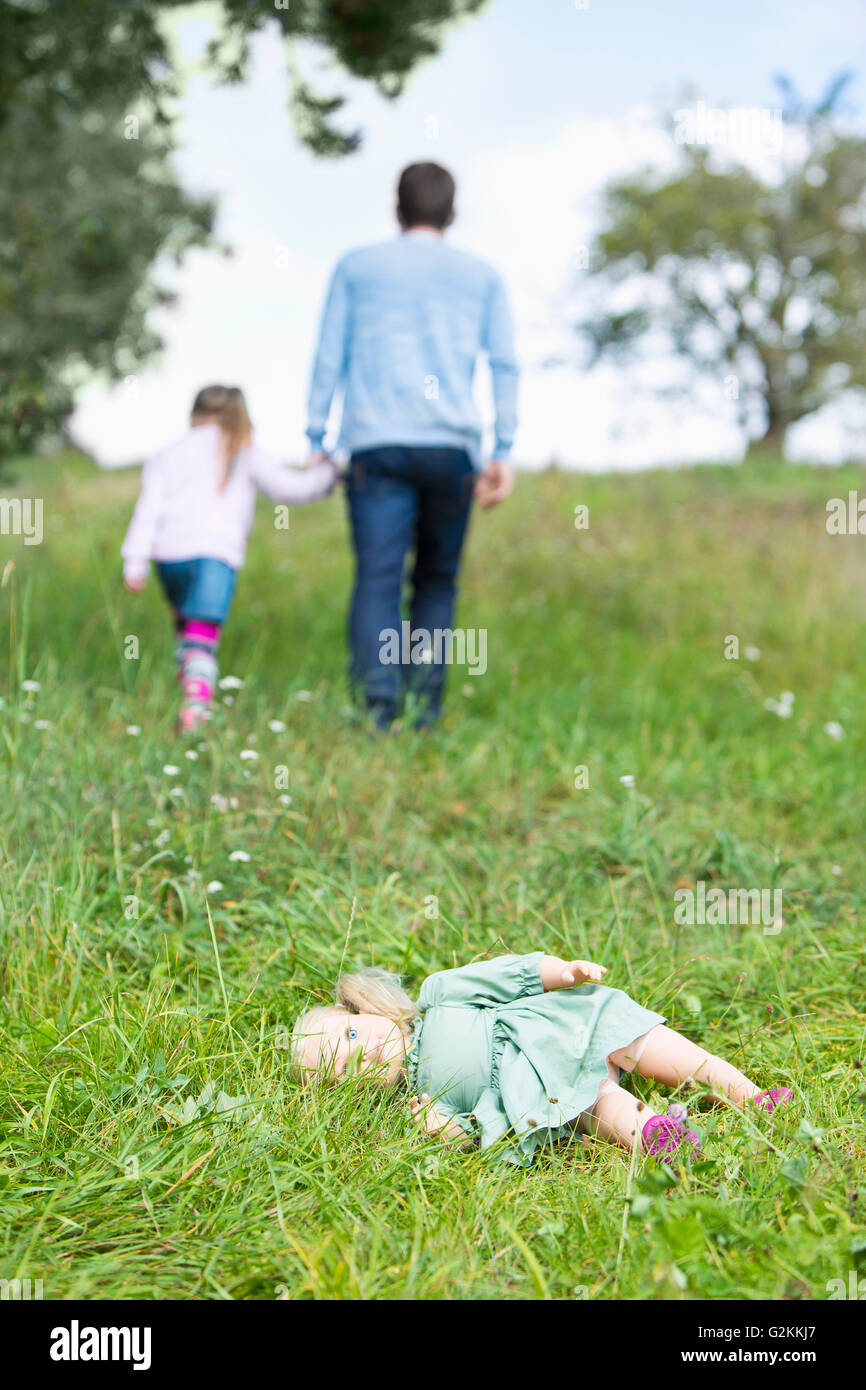 Doll lying on meadow while man going away with little girl Stock Photo