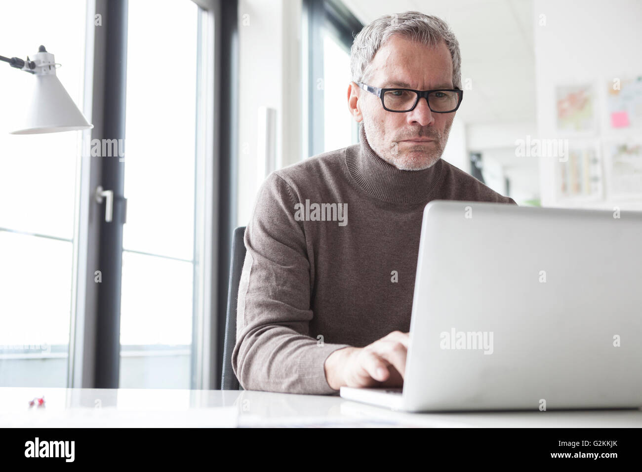 Mature man sitting in office using laptop Stock Photo
