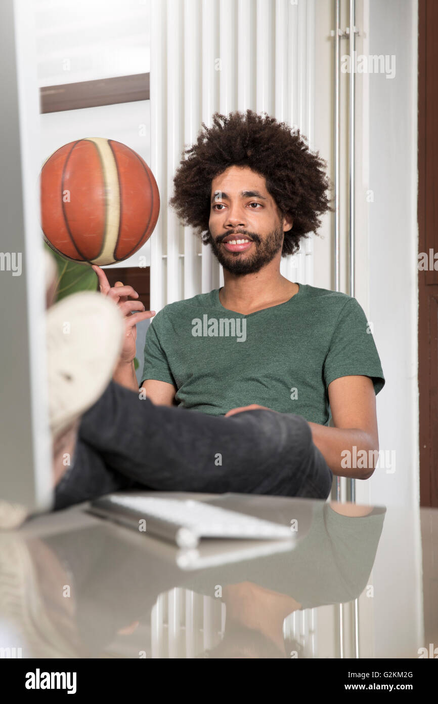 Creative professional balancing basketball at desk in office Stock