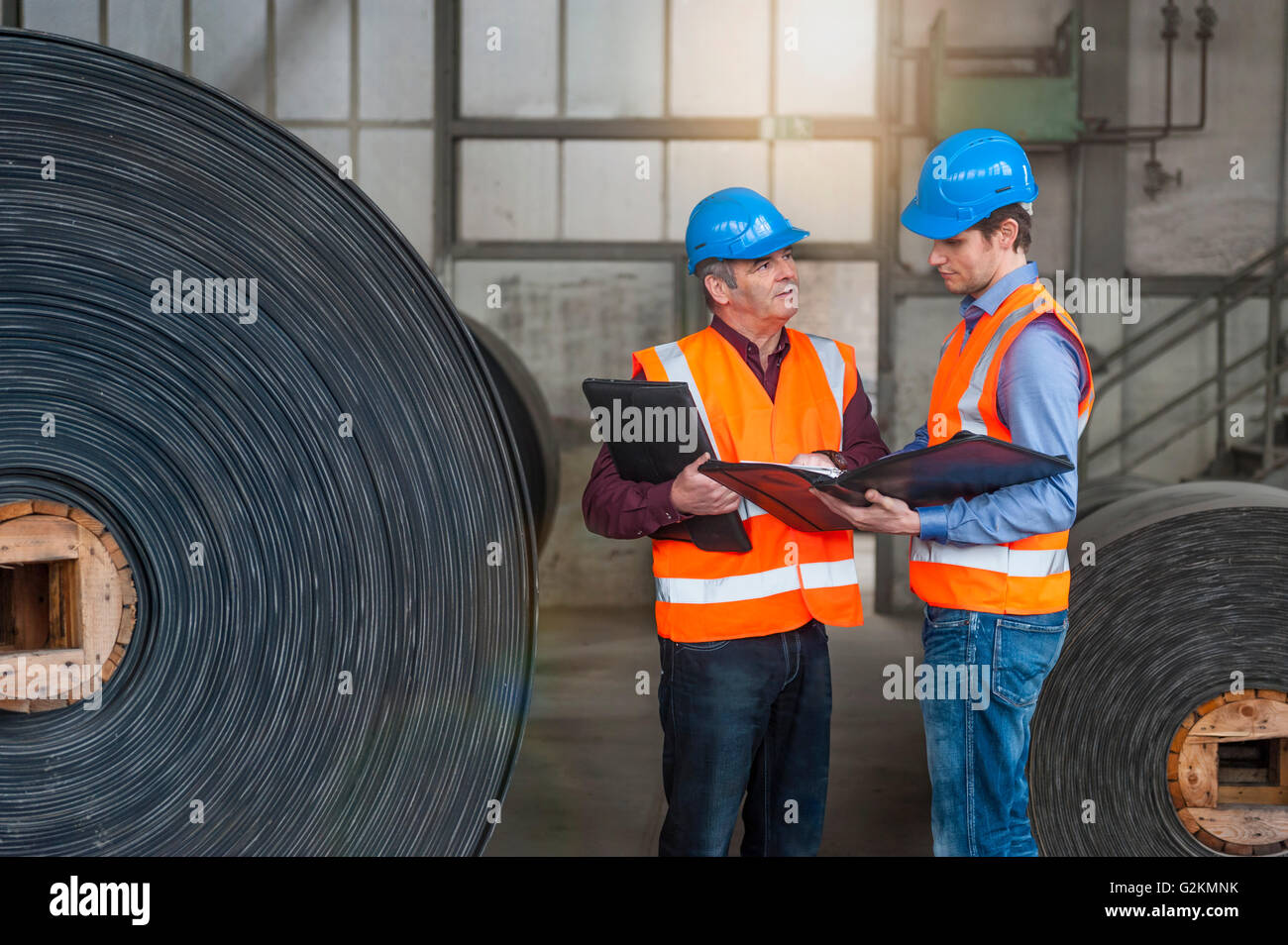 Two men with documents in factory hall with rolls of rubbe Stock Photo