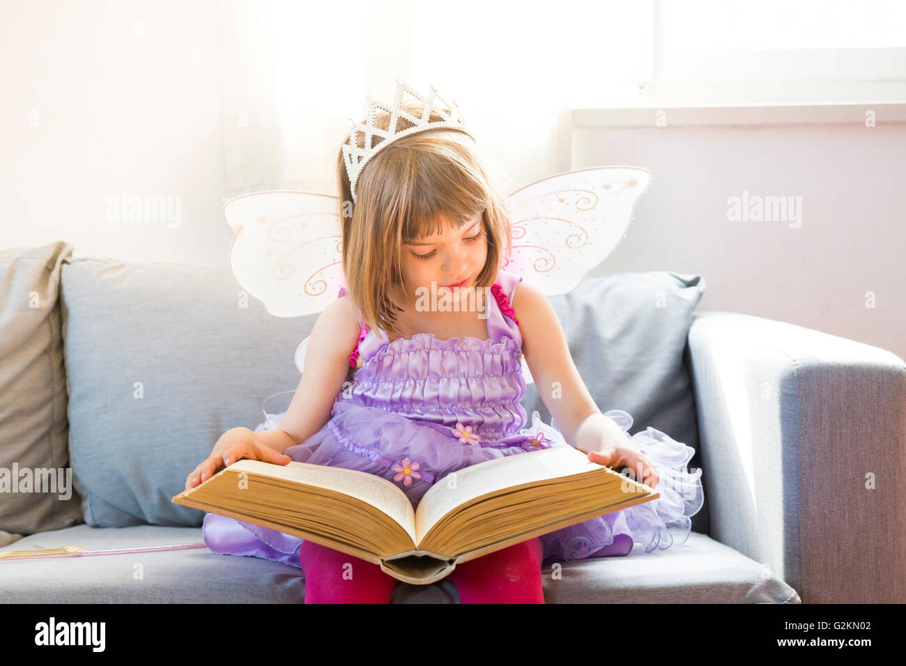 Portrait of little girl dressed up as fairy queen reading book Stock