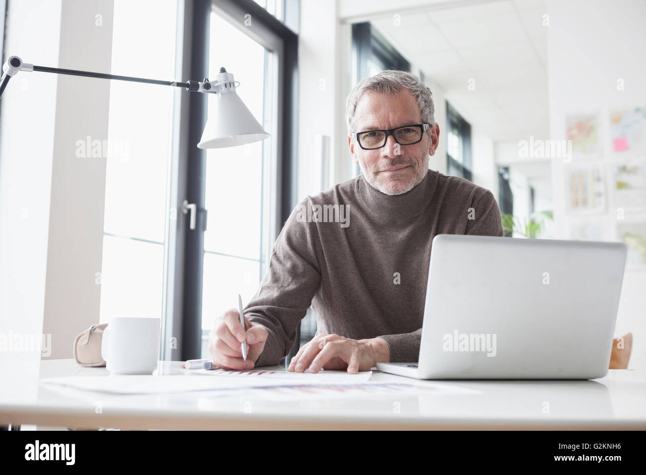 Mature man sitting in office using laptop Stock Photo