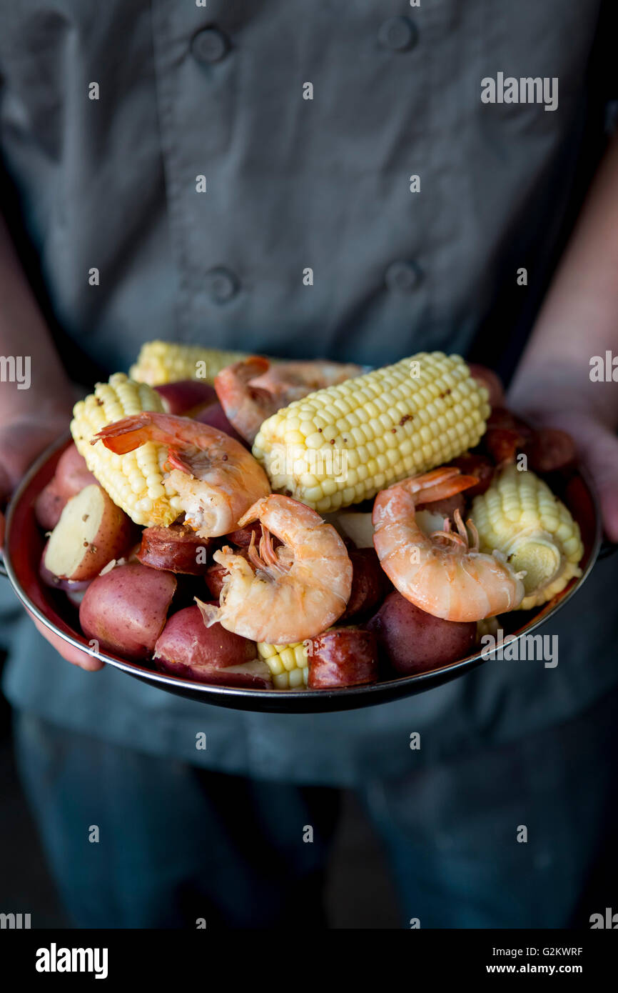 Chef Holding Plate of Low Country Boil with Shrimp, Corn, Potatoes and Sausage Stock Photo