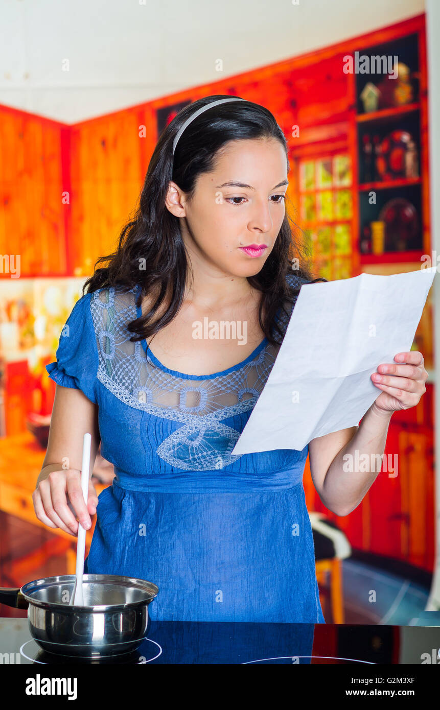 Woman looking to a written cooking recipe and holding a white spoon ...