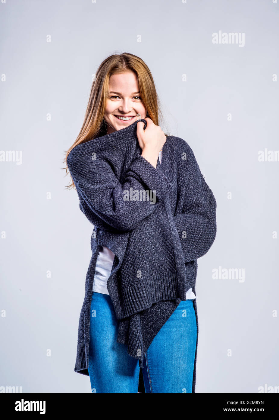 Teenage girl in jeans and long gray sweater, young woman, studio shot on gray background Stock Photo