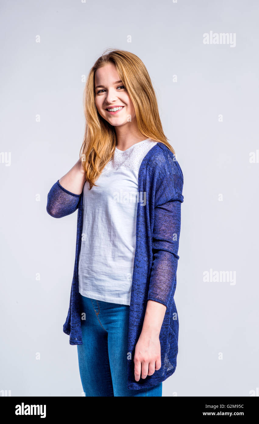 Teenage girl in jeans and long blue sweater, young woman, studio shot on gray background Stock Photo