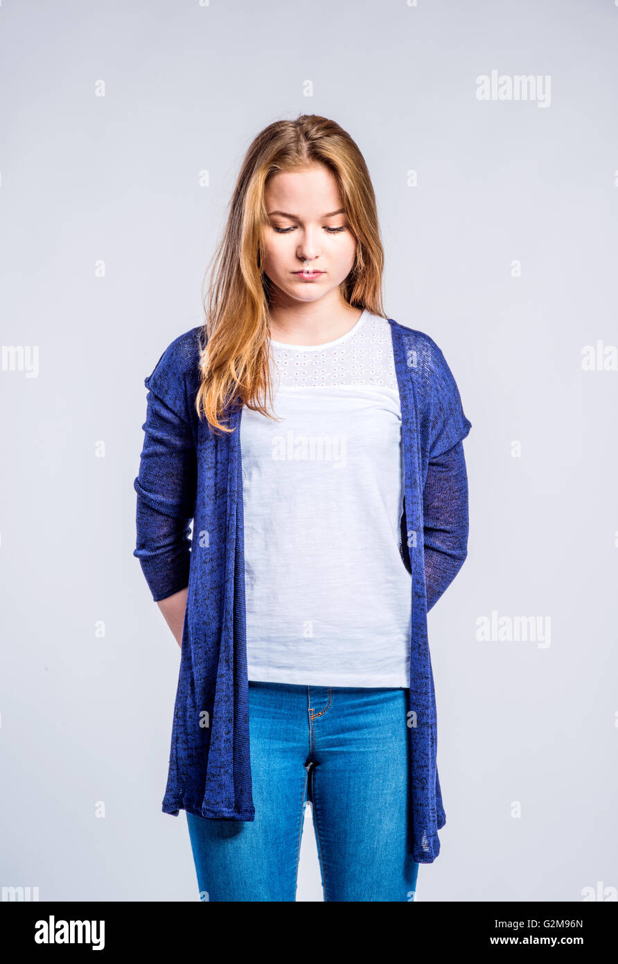 Teenage girl in jeans and long blue sweater, young woman, studio shot on gray background Stock Photo