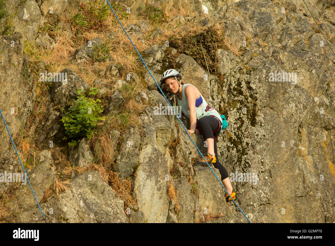 Female rock climber practicing on rocky cliff face at MaCauley Point park-Victoria, British Columbia, Canada. Stock Photo
