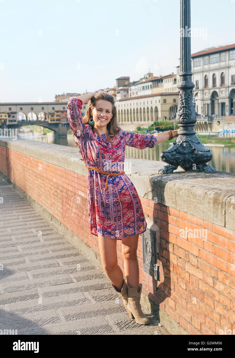 Remarkable holiday in Florence. Full length portrait of happy woman in a dress walking along the embankment near Ponte Vecchio Stock Photo