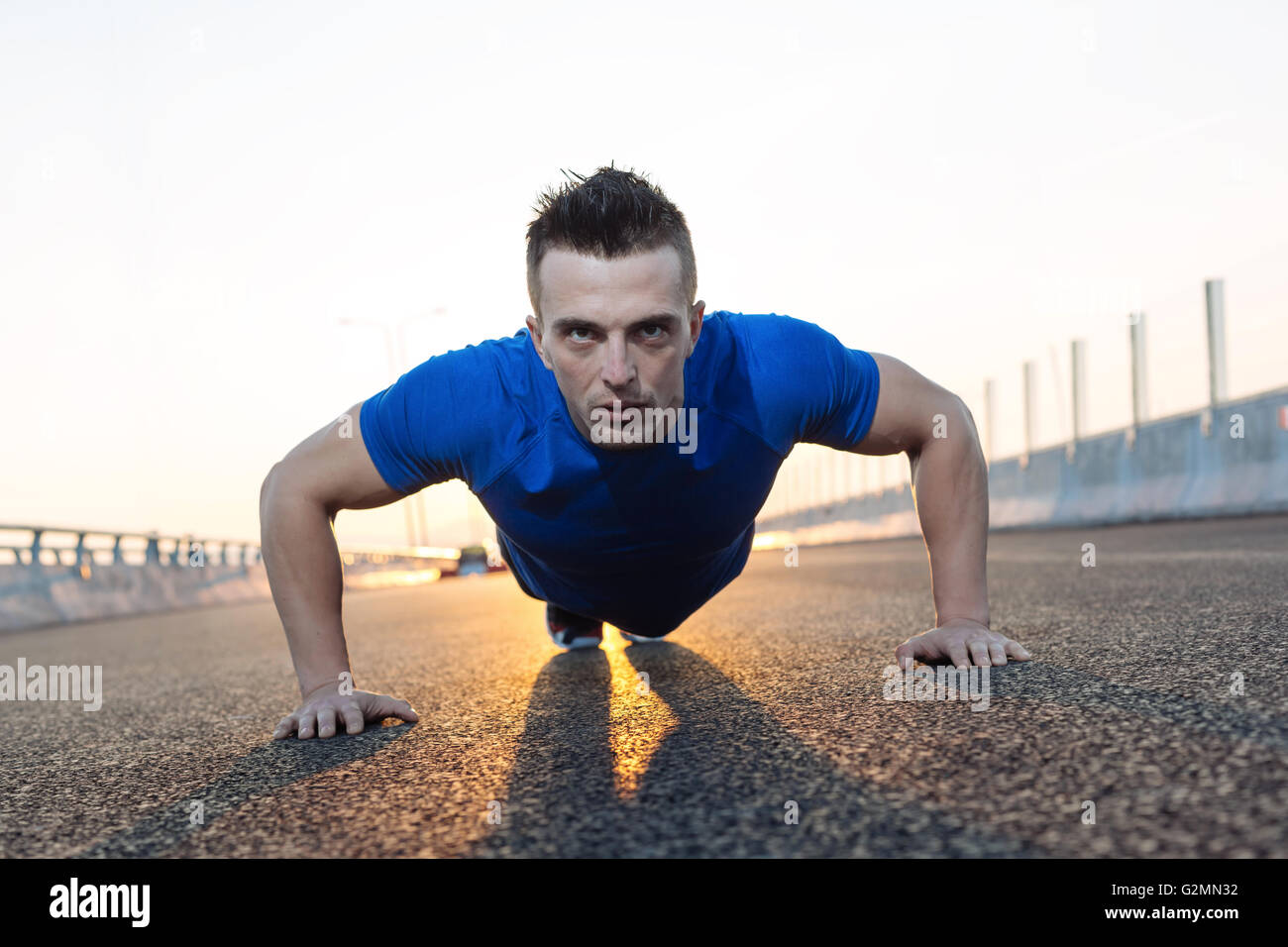 Handsome male runner doing pushups on stairs in urban setting, young