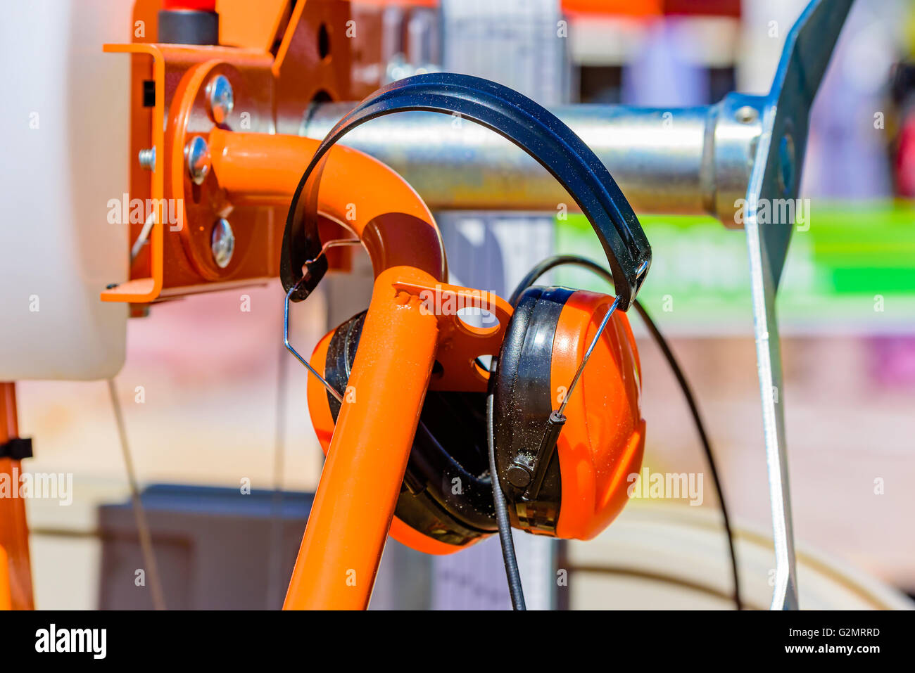 Orange hearing protections or earmuffs hanging on an orange machine part. Stock Photo