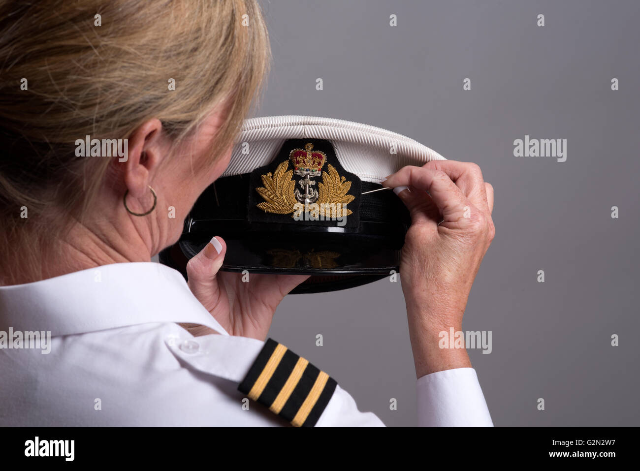 SEWING A NAVAL CAP BADGE ONTO A HAT Female officer sewing the cap badge onto a naval officer's uniform cap Stock Photo
