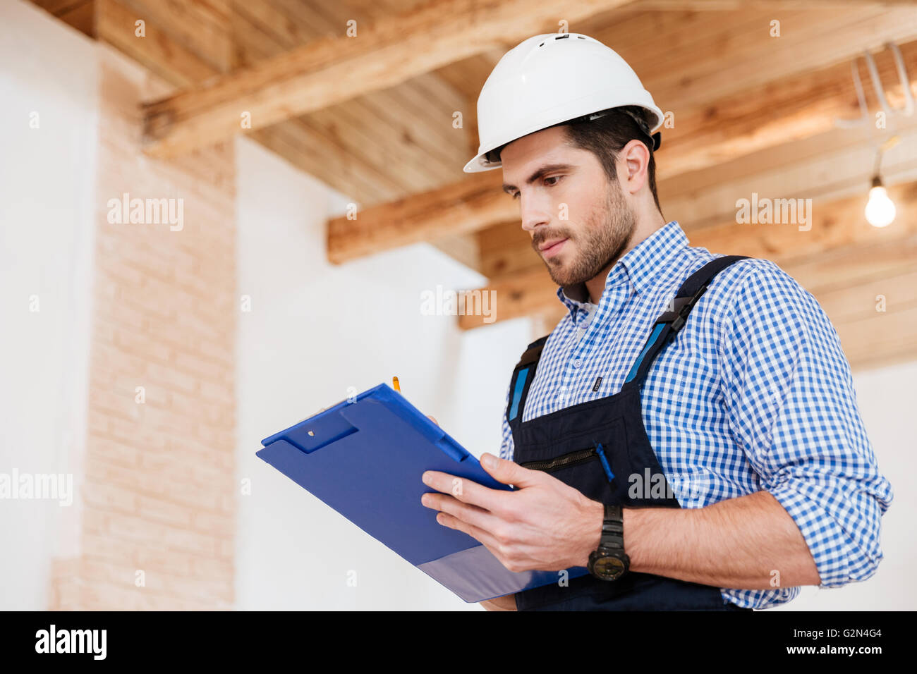 Happy builder writing something in hardhat with clipboard in his hands ...