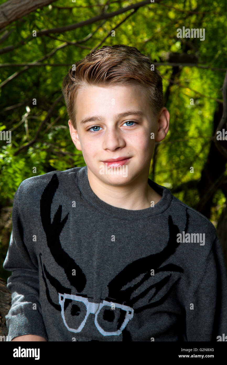 Portrait of a tween boy leaning on a tree with a cocky expression.  He has big, blue eyes, blond hair, and is wearing a  sweater Stock Photo