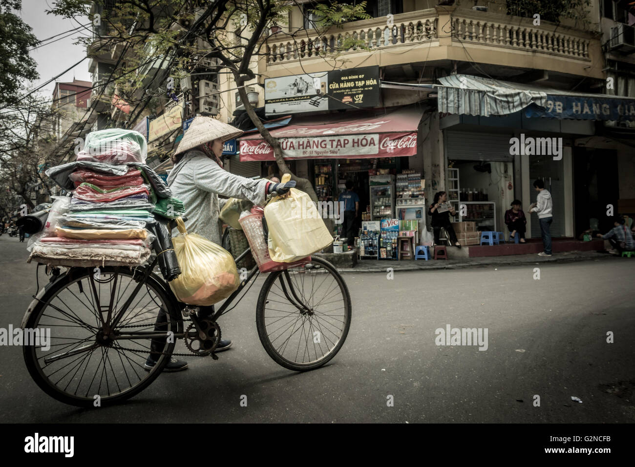 Vietnamese person with conical hat pushing a traditional bike in a typical street in Hanoi, Vietnam Stock Photo