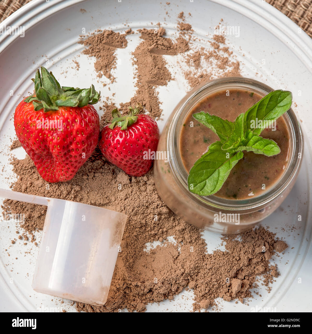 Powdered meal replacement shake looking down at jar, scoop, powder with strawberries and mint leaves Stock Photo