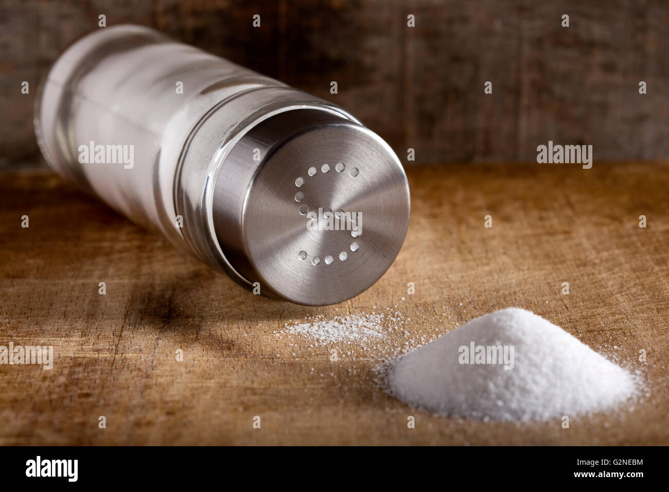 Lying down glass salt cellar and spilled salt on a wood background Stock Photo