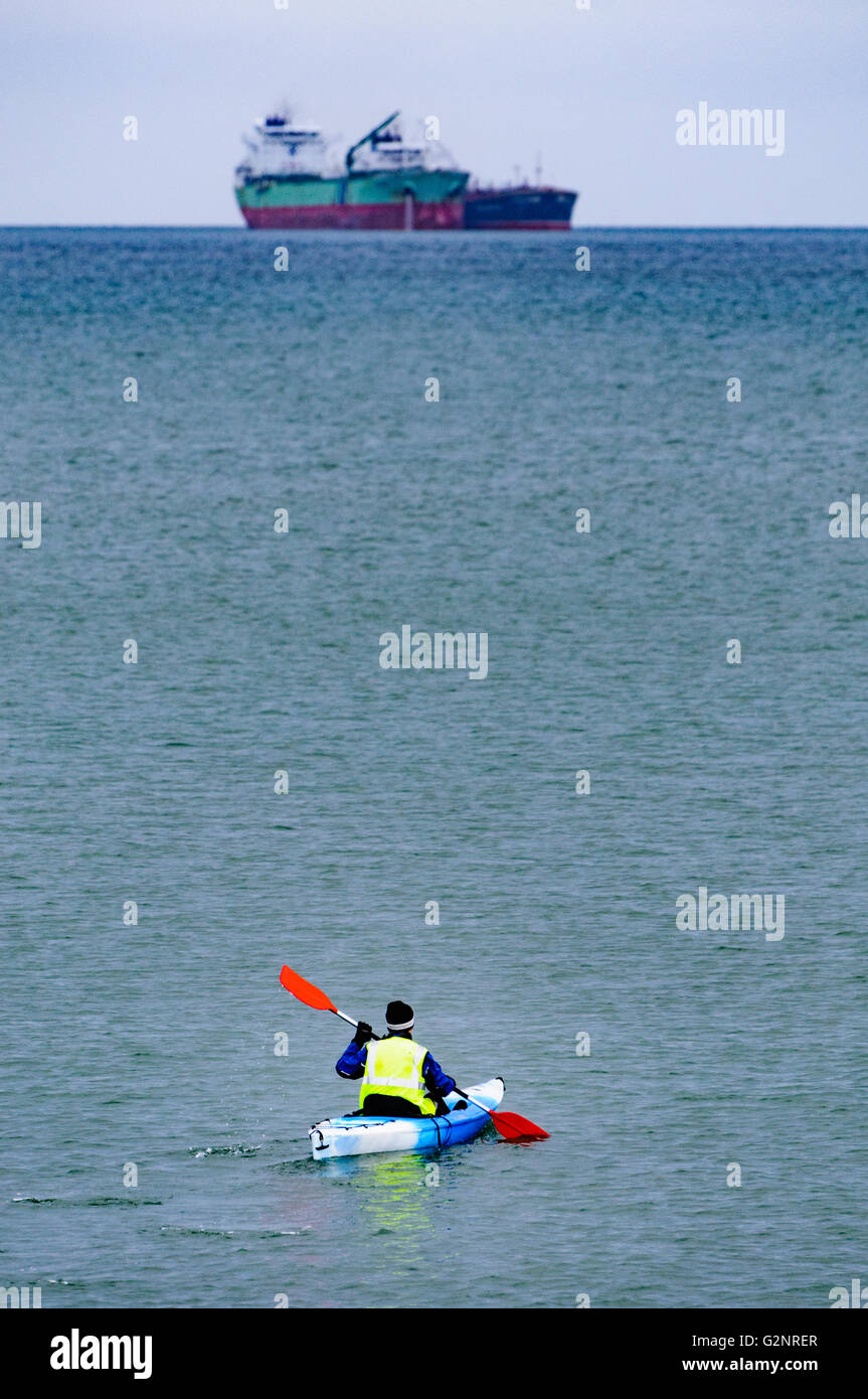Belfast, Northern Ireland. 07/01/2012: A man in a kayak canoe paddles towards two oil tankers anchored far out at sea. Stock Photo