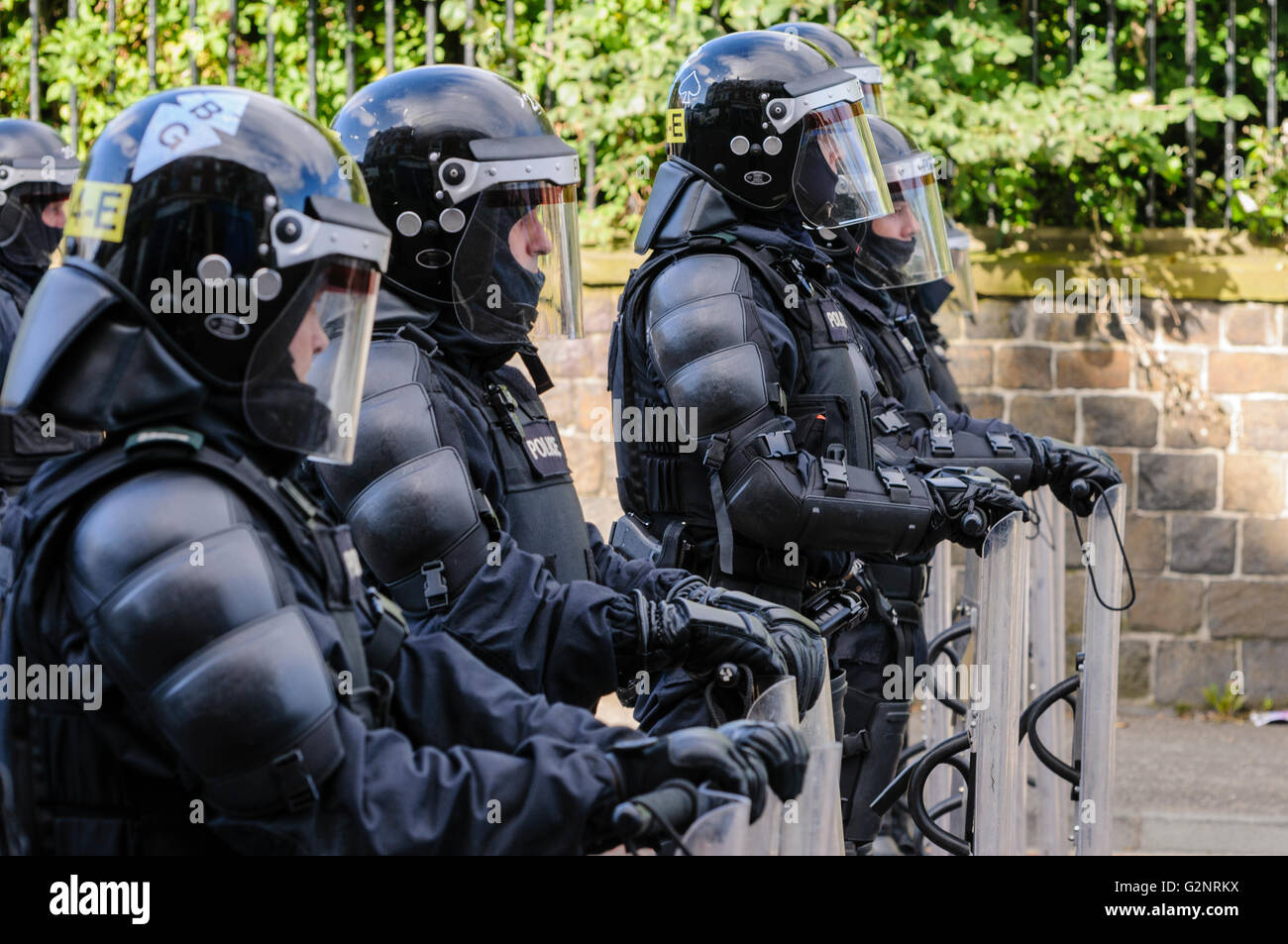 PSNI police officers in riot gear, including helmets and shields, line up across a road to block it from a crowd. Stock Photo