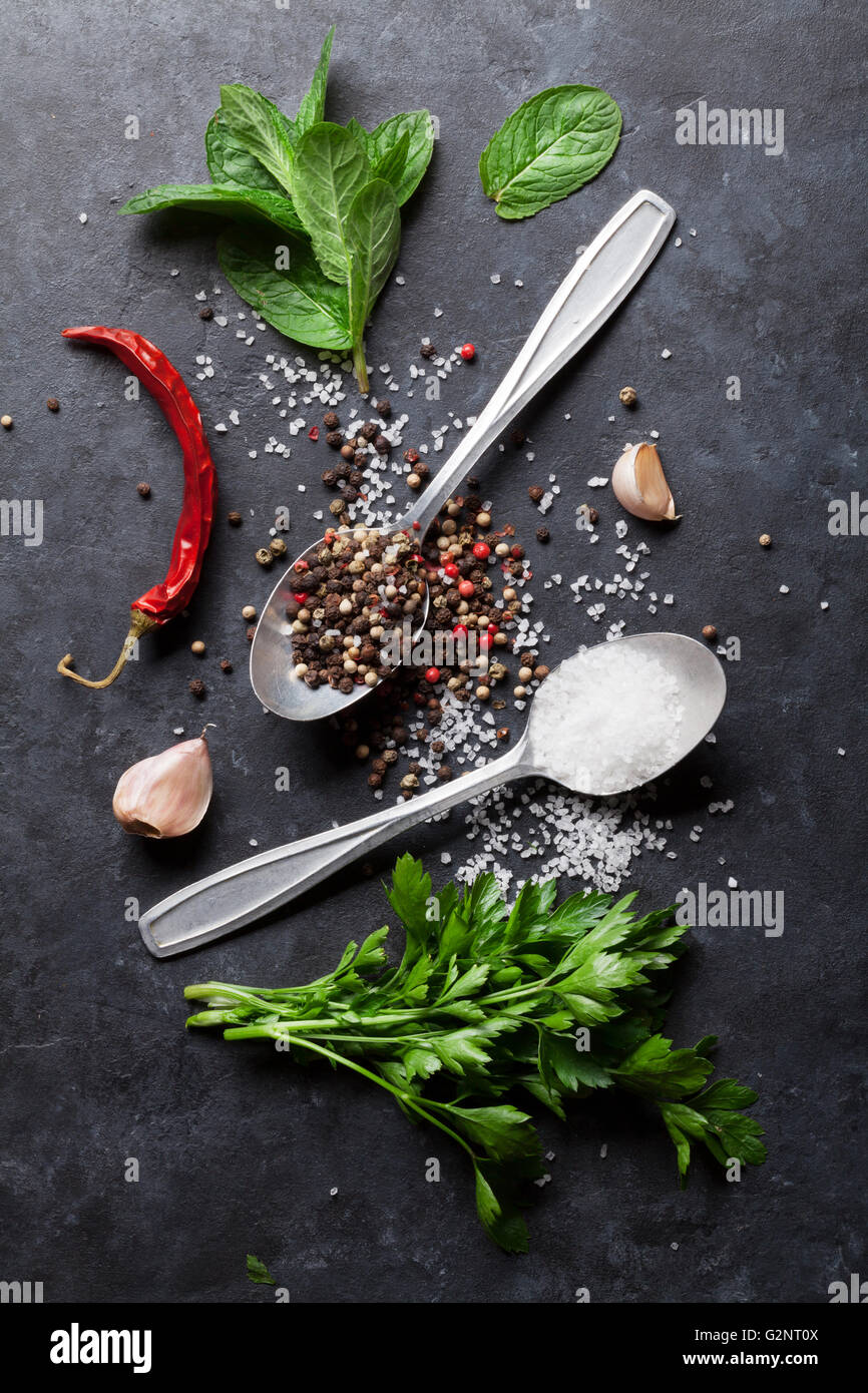 Black, white and red pepper and salt spices in spoon. Mint and parsley herbs. Top view Stock Photo
