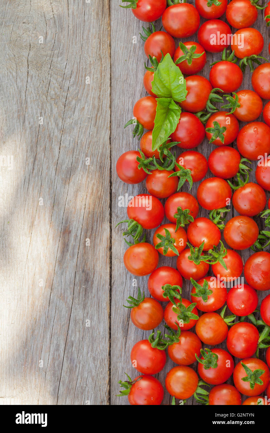 Ripe cherry tomatoes texture and basil leaves on wooden table. Top view ...