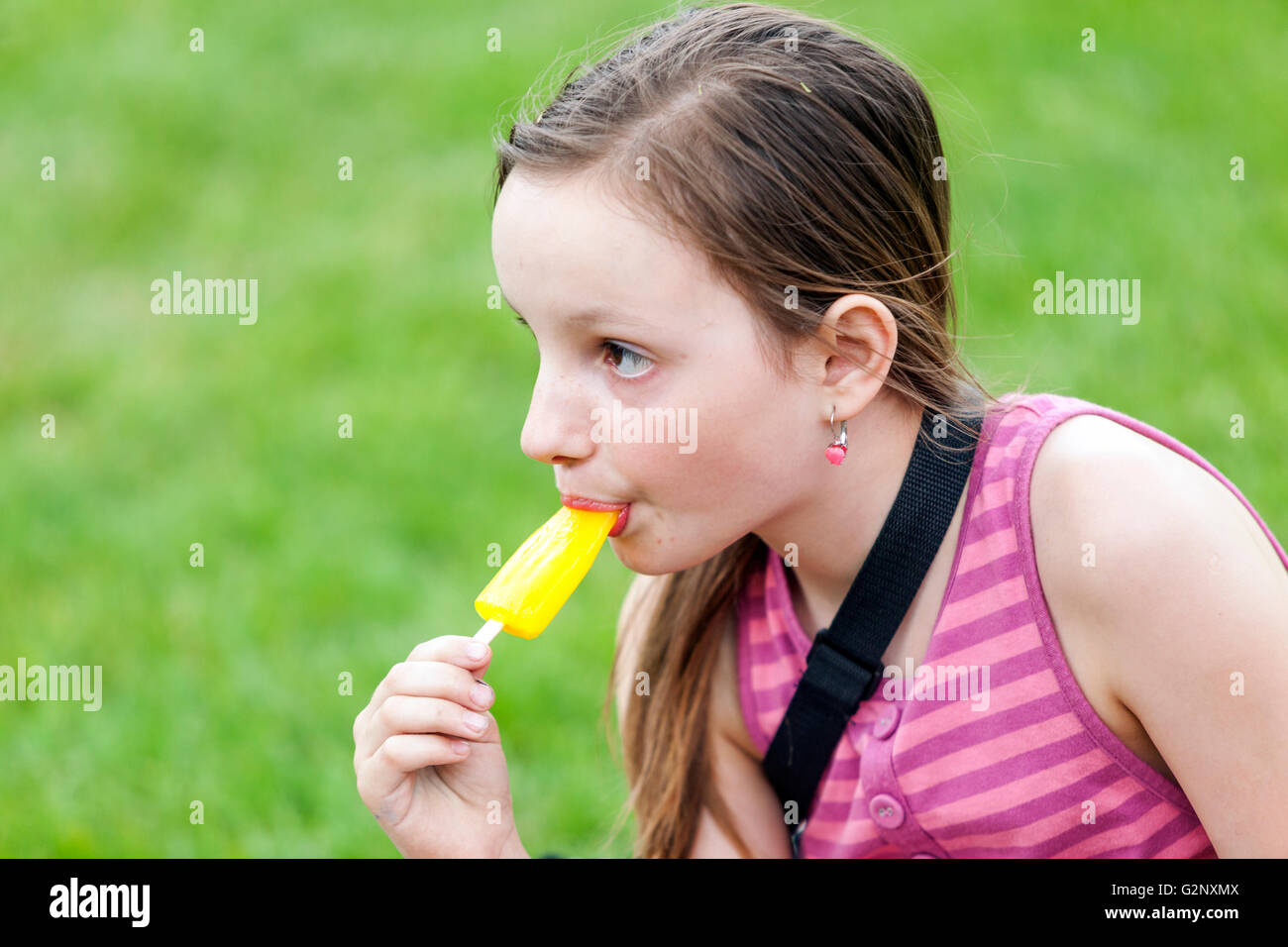 young girl tasting and sucking frozen yellow ice cream on a stick Stock Photo