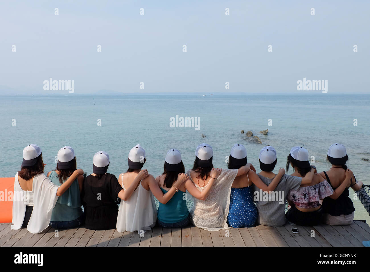 group of ten women friends sit hug together look at blue sea sky. seascape Stock Photo