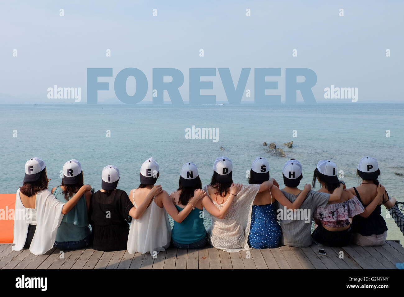 group of ten women friends sit hug together look FOREVER blue sea sky Stock Photo