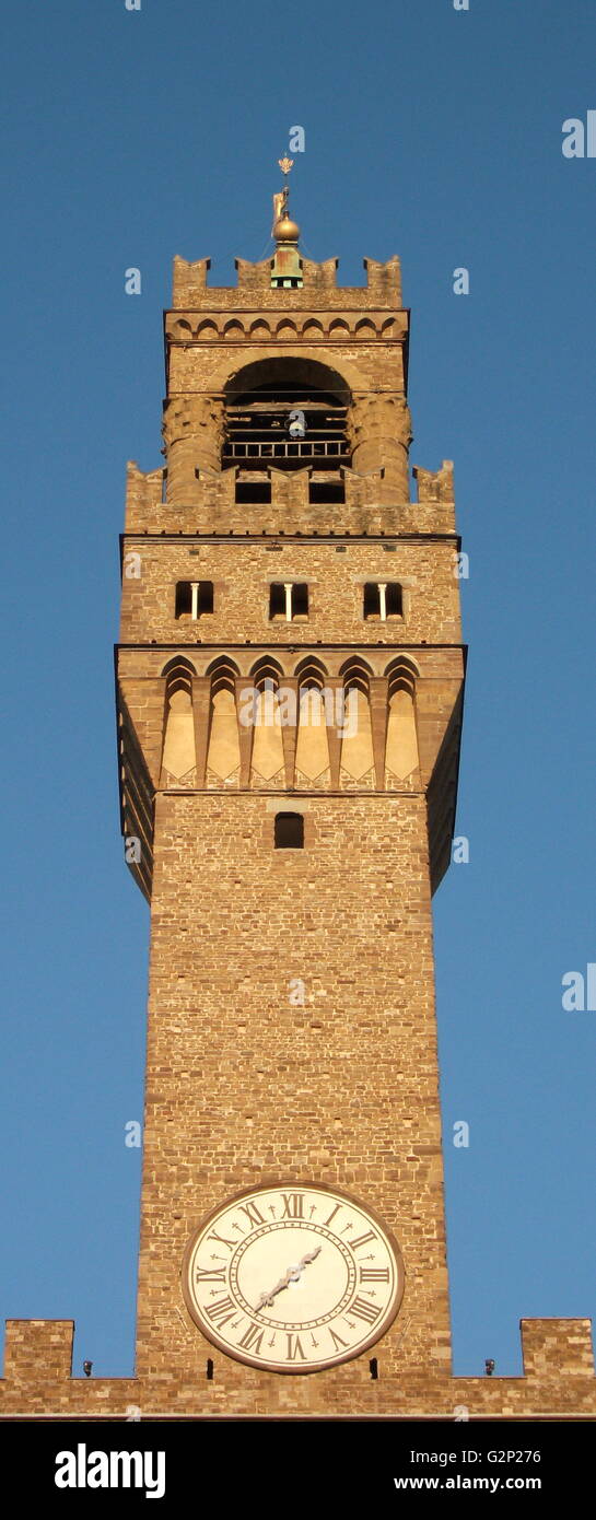 The clock tower of the Palazzo Vecchio. Town hall of Florence, Italy. A huge Romanesque fortress-palace overlooking the Piazza della Signoria. Designed by the architect Arnolfo di Cambio in 1299. A stonework cubicle building forms the base, crowned with a projected battlement clock tower. The current clock was made by Vincenzo Viviani in 1667. Arches in the structure are decorated with the 9 coats of arms of the Florentine Republic. Stock Photo