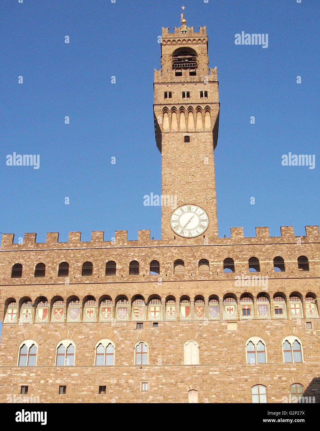 The Palazzo Vecchio. Town hall of Florence, Italy. A huge Romanesque fortress-palace overlooking the Piazza della Signoria. Designed by the architect Arnolfo di Cambio in 1299. A stonework cubicle building forms the base, crowned with a projected battlement clock tower. The current clock was made by Vincenzo Viviani in 1667. Arches in the structure are decorated with the 9 coats of arms of the Florentine Republic. Stock Photo