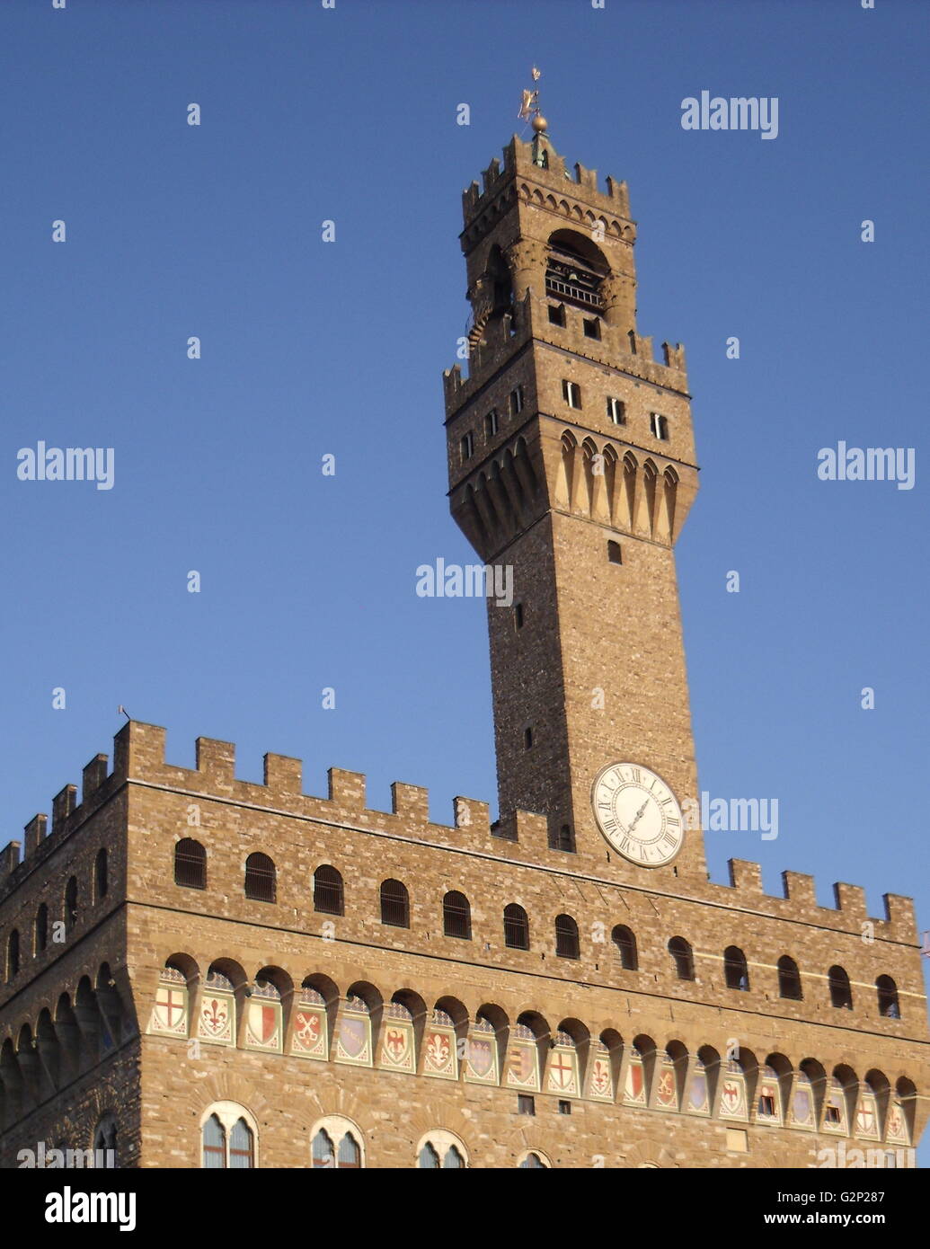 The Palazzo Vecchio. Town hall of Florence, Italy. A huge Romanesque fortress-palace overlooking the Piazza della Signoria. Designed by the architect Arnolfo di Cambio in 1299. A stonework cubicle building forms the base, crowned with a projected battlement clock tower. The current clock was made by Vincenzo Viviani in 1667. Arches in the structure are decorated with the 9 coats of arms of the Florentine Republic. Stock Photo