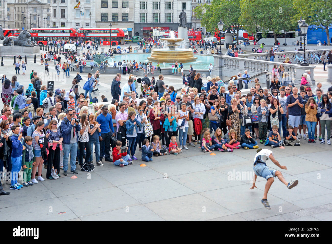 Large crowd of people including tourists gather around street performer gymnastic dancing in front of spectators in Trafalgar Square London England UK Stock Photo