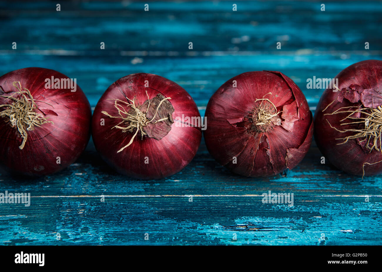 Whole Red Onions on Cyan Blue Wooden Board Stock Photo