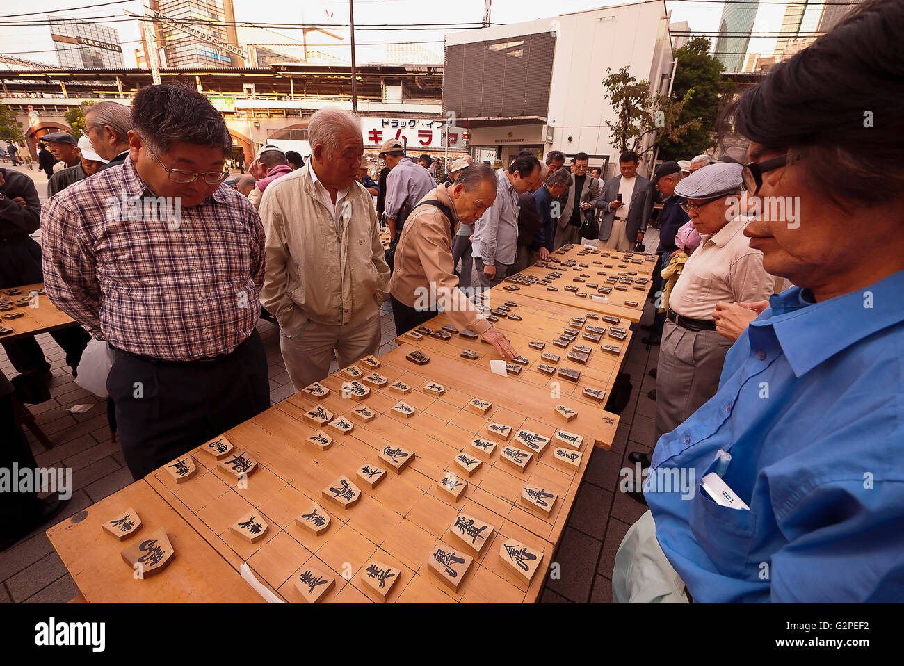 Shimbashi, Outside Shimbashi JR station, large group of men, all over fifty years old, playing Shogi, Japanese chess, on large boards with large pieces, all standing, other men watch. Stock Photo