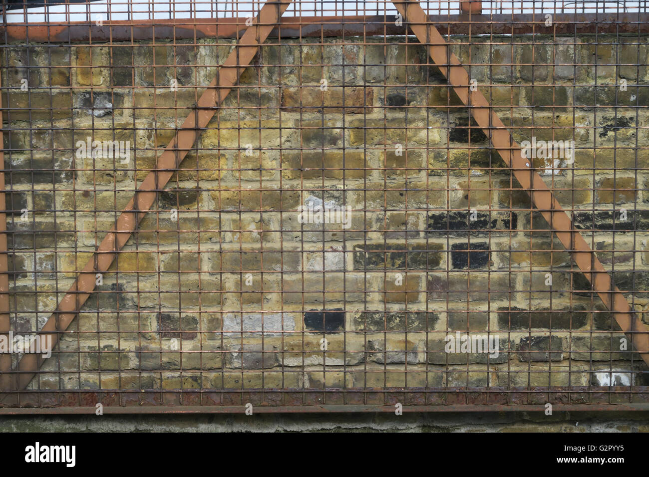 rusted metal wire gate closed over an aged brick wall Stock Photo